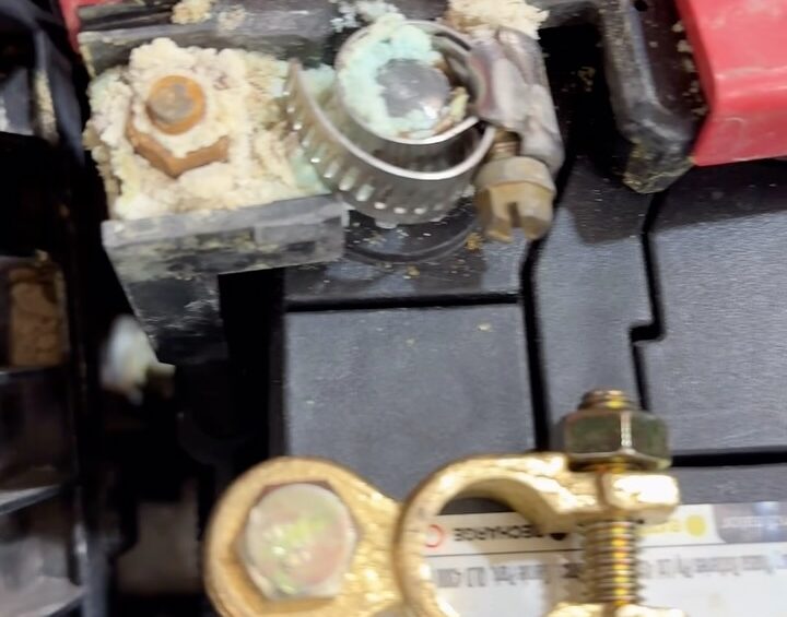 Corroded car battery terminal held together with a hose clamp, next to a new terminal