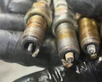 Three oil-soaked spark plugs from a Renault Kangoo, one with its centre electrode melted away