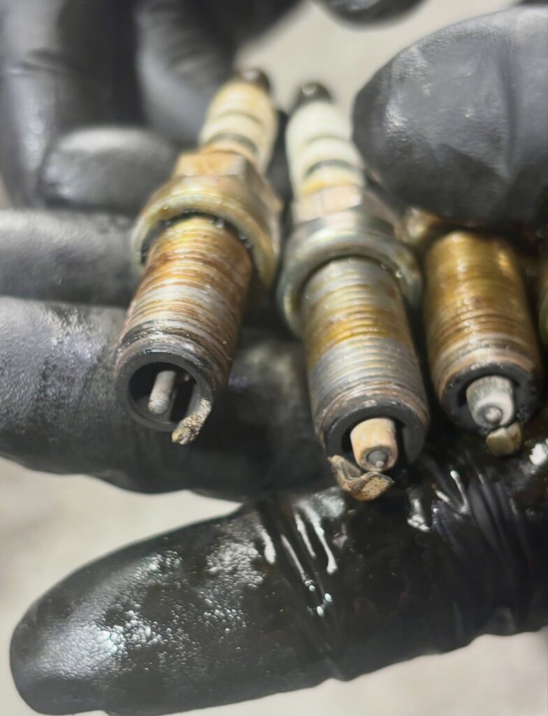 Three oil-soaked spark plugs from a Renault Kangoo, one with its centre electrode melted away